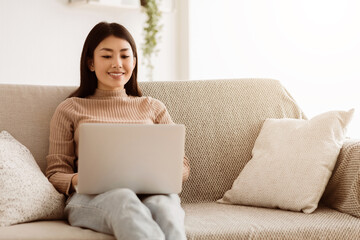 Wall Mural - Modern Job Lifestyle. Young Girl Sitting on Sofa at Home Working on Laptop Online, Using Internet, Free Space