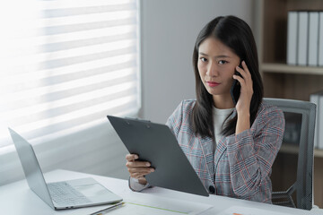 Sharing good business news. Attractive young businesswoman talking on the mobile phone and smiling while sitting at her working place in office and looking at laptop PC.