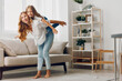 © SHOTPRIME STUDIO - Mother carrying daughter on her back in cozy living room with sofa, coffee table, and warm lighting