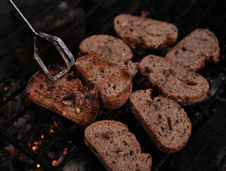 White bread toasted on an outdoor grill. Picnic outside. Turn over pieces of fried bread using iron tongs.