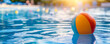© MCGORIE - Colorful beach ball floating in the water of an outdoor swimming pool, with sunlight creating a soft glow on its surface and reflecting off the blue waters.