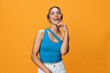 © SHOTPRIME STUDIO - Vibrant and joyful portrait of a laughing woman in blue top and white jeans on orange background