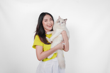 Wall Mural - Smiling young Asian woman in yellow shirt is holding a white ragdoll cat over isolated white background.