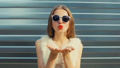 Wall Mural - Modern stylish young woman blowing kiss in white glasses, fashionable girl posing on gray background
