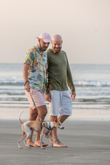 couple of homosexual men walking their dog on the beach at sunrise