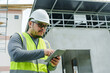 © Ekkasit A Siam - Asian male engineer in white hard hat and reflective vest using tablet at construction site. Focused on project details. Partially constructed building in background. Professional and engaged.