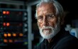 © imagineRbc - A man with a white beard and glasses is looking at the camera. He is standing in front of a server rack, which is out of focus in the background