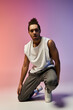 © LIGHTFIELD STUDIOS - A young African American man in a white sleeveless shirt and grey pants poses on one knee against a bright, colorful gradient background.