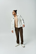 © LIGHTFIELD STUDIOS - A young African American man poses in a stylish white jacket and brown pants against a gray background.