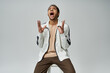 © LIGHTFIELD STUDIOS - A young African American man is in a stylish white jacket and brown pants against a grey background.