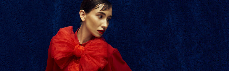 Wall Mural - A young woman with short hair poses in a vibrant red outfit against a rich blue backdrop.