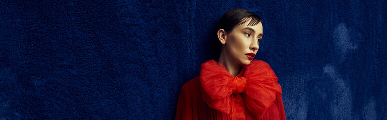 Wall Mural - A young woman with short hair poses in a red dress with a large bow against a blue background.