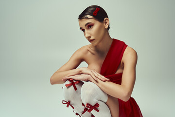 Wall Mural - A young woman with short hair poses in a red crop top and mini skirt against a grey backdrop.