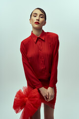 Wall Mural - A young woman in a red dress with a bow poses against a gray background.