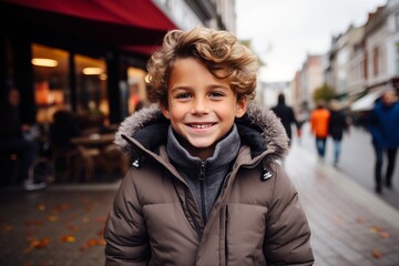 Poster - Outdoor portrait of cute little boy with blond curly hair, wearing warm coat, looking at camera and smiling.