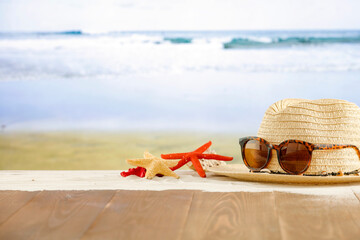 Wall Mural - Straw hat and sunglasses and starfish on wooden table top on a tropical beach with and sea background.