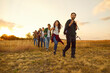 © Studio Romantic - Group of young friends tourists trekking with backpacks walking in a row in the field. Happy people men and women on a hiking trip holiday in nature at sunset. Adventure, travel and tourism concept.