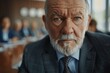 © ChaoticMind - A stern-looking elderly businessman with a beard is sitting at a meeting table in a modern office, expressing authority and focus in a professional corporate setting.
