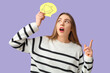 © Pixel-Shot - Excited young woman raising index finger and holding speech bubble with drawn bell on lilac background. Reminder concept