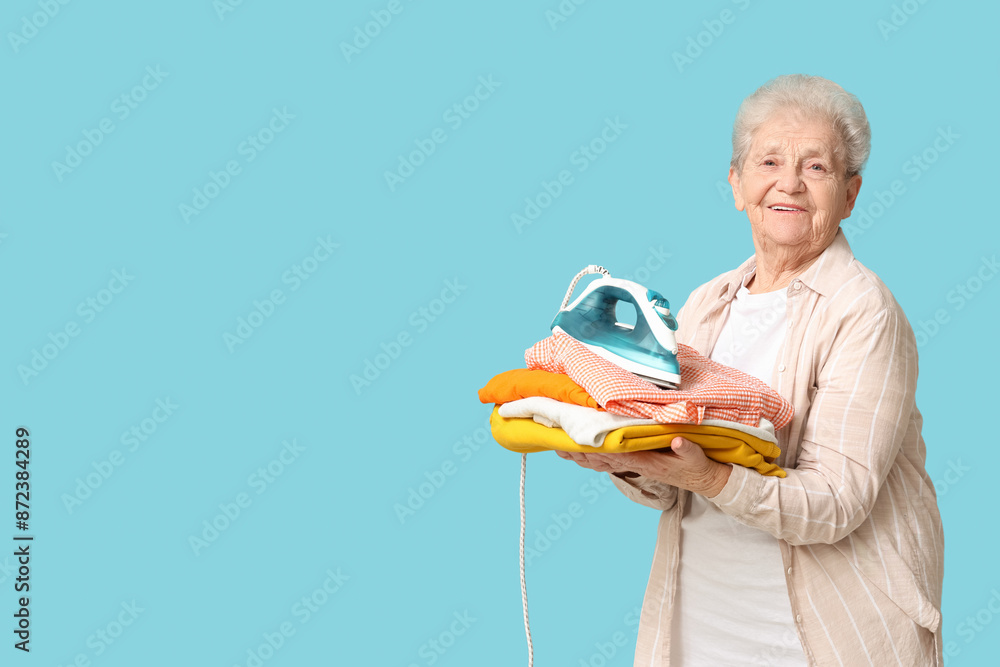 Happy senior woman with iron and stack of laundry on blue background