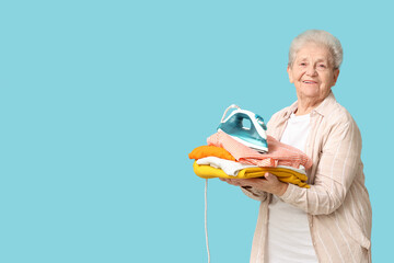 Wall Mural - Happy senior woman with iron and stack of laundry on blue background