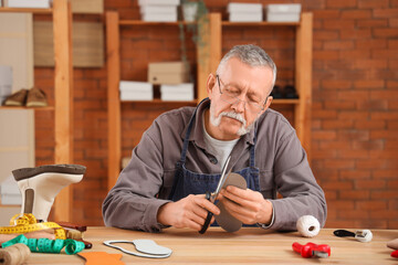 Sticker - Male shoemaker cutting insole at table in workshop