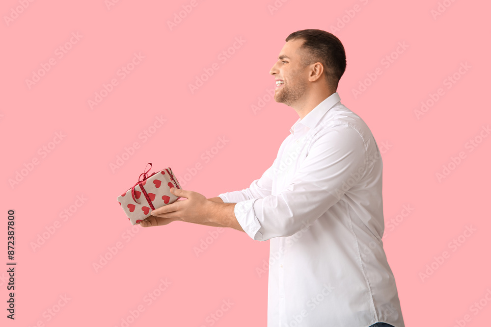 Handsome young happy man with gift box on pink background