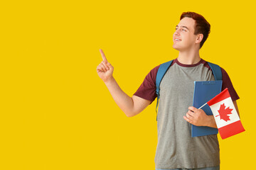 Canvas Print - Male student with flag of Canada and clipboard on yellow background