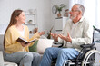 © Pixel-Shot - Senior man in wheelchair talking to caregiver with book at nursing home