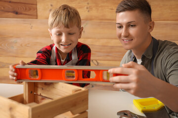 Canvas Print - Male worker with level and his little son measuring wooden box in workshop