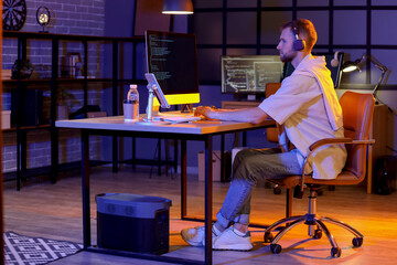 Poster - Young bearded programmer with headphones working in office at night