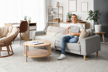 Sticker - Young man with weight scales sitting on sofa at home