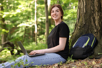 Wall Mural - Smiling freelancer working with laptop in forest. Remote job