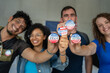 © Alan - diverse group of smiling friends holding 2024 Vote election I voted buttons or pins at a US election polling station. In the background, american flag at the background, democracy in America USA