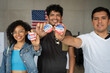 © Alan - group of Hispanic smiling people holding 2024 Vote election I voted buttons or pins at a US election polling station. In the background, american flag at the background, concept of latin, latino vote