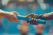 © Khawla - Passing the Relay Baton. Close-up of two hands passing the baton in a track and field race, A blurred background of a sports stadium