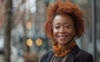 © imagineRbc - A smiling mature Black woman wearing a colorful scarf stands outside in a city setting