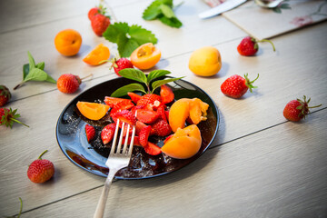 Wall Mural - fresh fruit salad of ripe strawberries and apricots, on a light wooden table