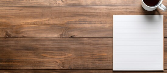 Wall Mural - Wooden desk in an office setting featuring a blank notepad, pen, and coffee cup on it. Top-down flat lay view with available space for adding an image. with copy space image