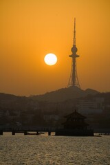 Poster - Sunset over Qingdao with the TV tower and traditional pavilion silhouetted against an orange sky