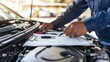 © somchit - Car maintenance expert inspecting the engine bay and documenting observations on a checklist