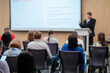 © Anton Gvozdikov - Audience attentively listening to a speaker presenting at a tech conference. Presenter in the background, highlighting modern business and technology topics.