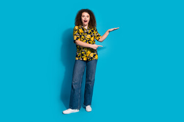 Wall Mural - Full length photo of cheerful excited lady dressed print shirt measuring arm pointing empty space isolated blue color background