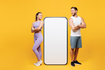Wall Mural - Full body young strong fitness trainer sporty two man woman wear blue clothes spend time in gym big blank screen area mobile cell phone isolated on plain yellow background. Workout sport fit concept.