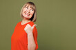 © ViDi Studio - Side view elderly blonde woman 50s years old wear orange t-shirt casual clothes point thumb finger aside on area mock up isolated on plain pastel green background studio portrait. Lifestyle concept.