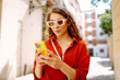 © maxbelchenko - Attractive woman tourist walking on city street using smartphone, browsing Internet on a phone, texting and communicating outdoors. Travel, blogging, weekend, relax and lifestyle concept.