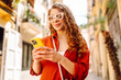 © maxbelchenko - Attractive woman tourist walking on city street using smartphone, browsing Internet on a phone, texting and communicating outdoors. Travel, blogging, weekend, relax and lifestyle concept.