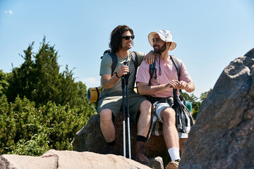 A gay couple enjoys a summer hike, taking a break to admire the view from a rocky outcrop.