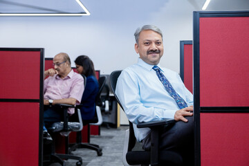 senior indian professional man working in corporate office and looking at camera. business and workspace concept.