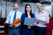 © GAJENDRRA BHATI  - Young Indian professional woman standing with laptop and two senior businessman besides her in corporate office. entrepreneur and workplace concept.